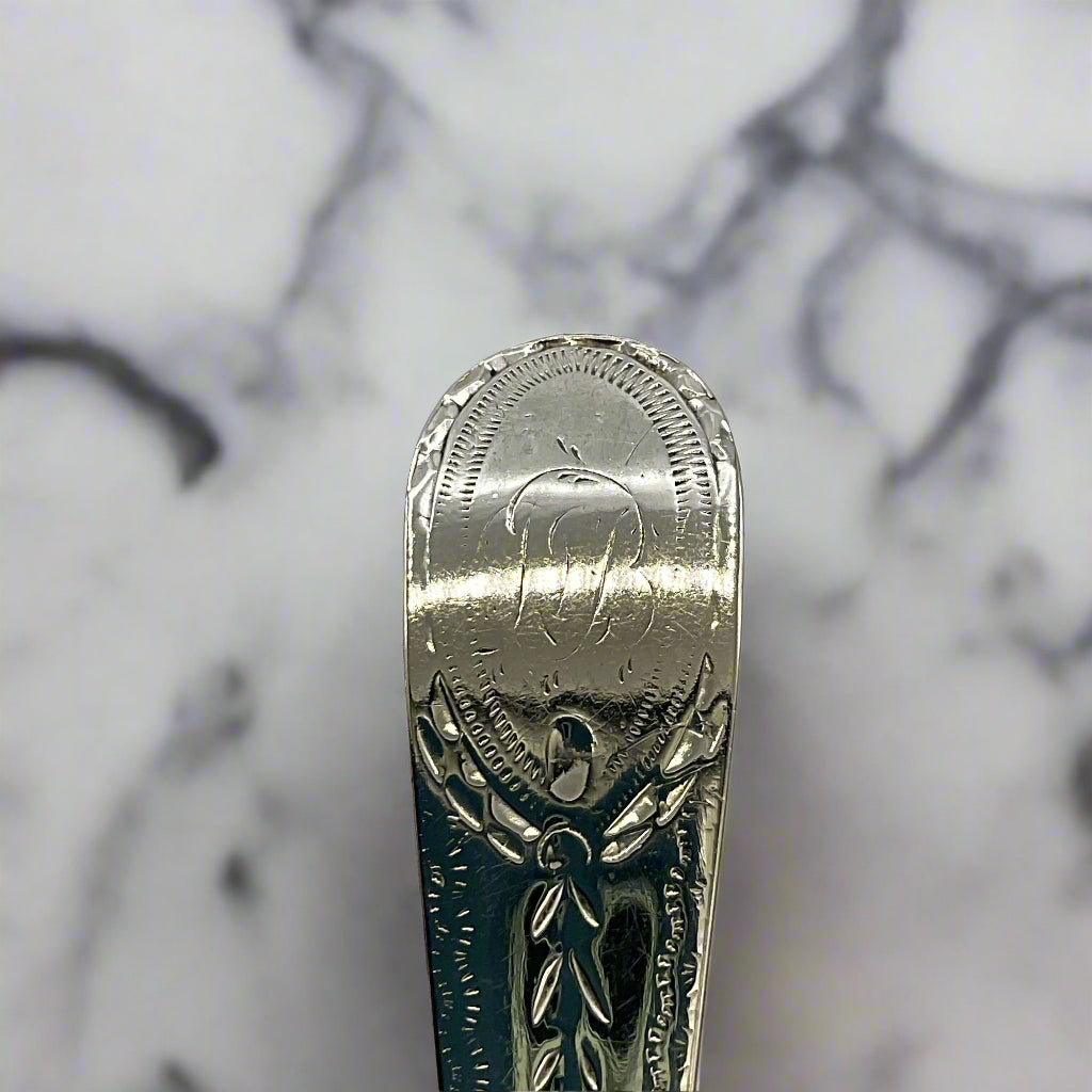 Silver spoon with intricate designs and engraved initials on a marble background 