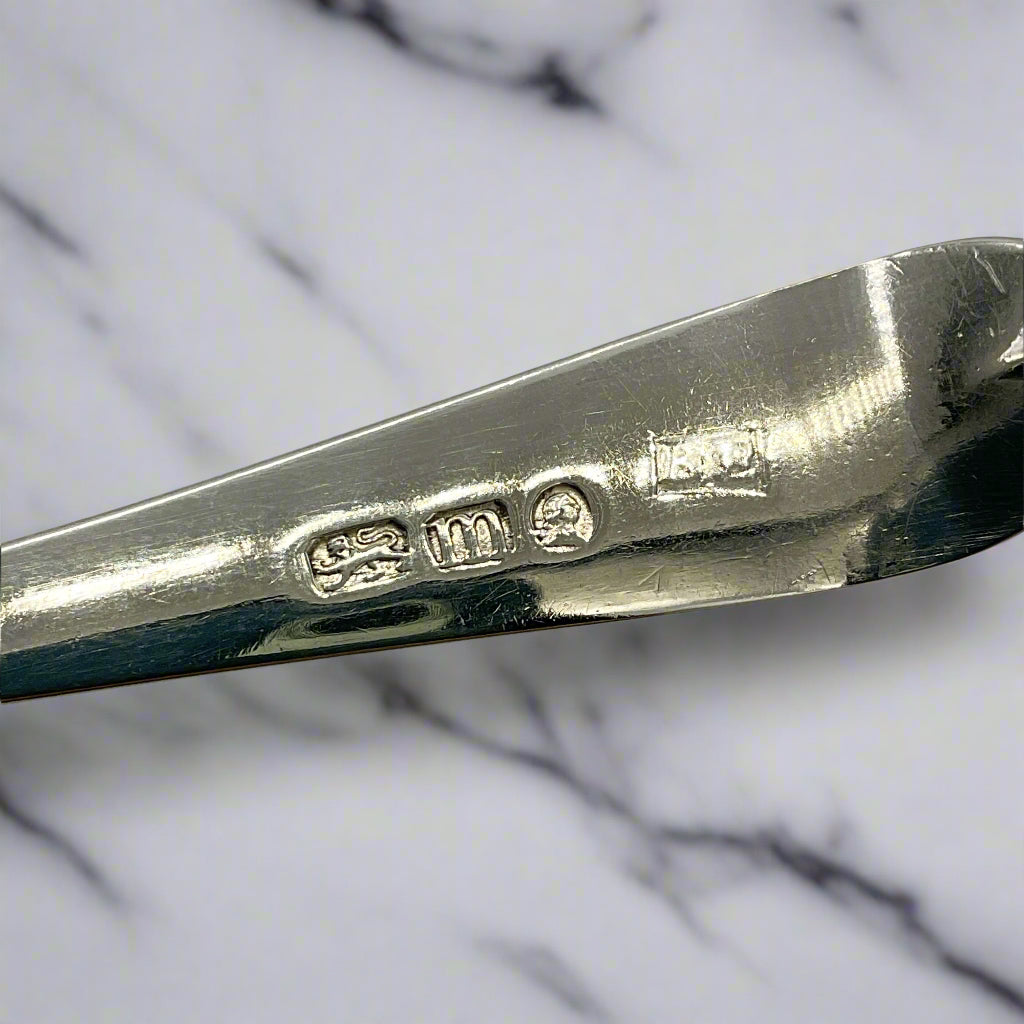 Close-up of a silver spoon with visible hallmarks on a marble background