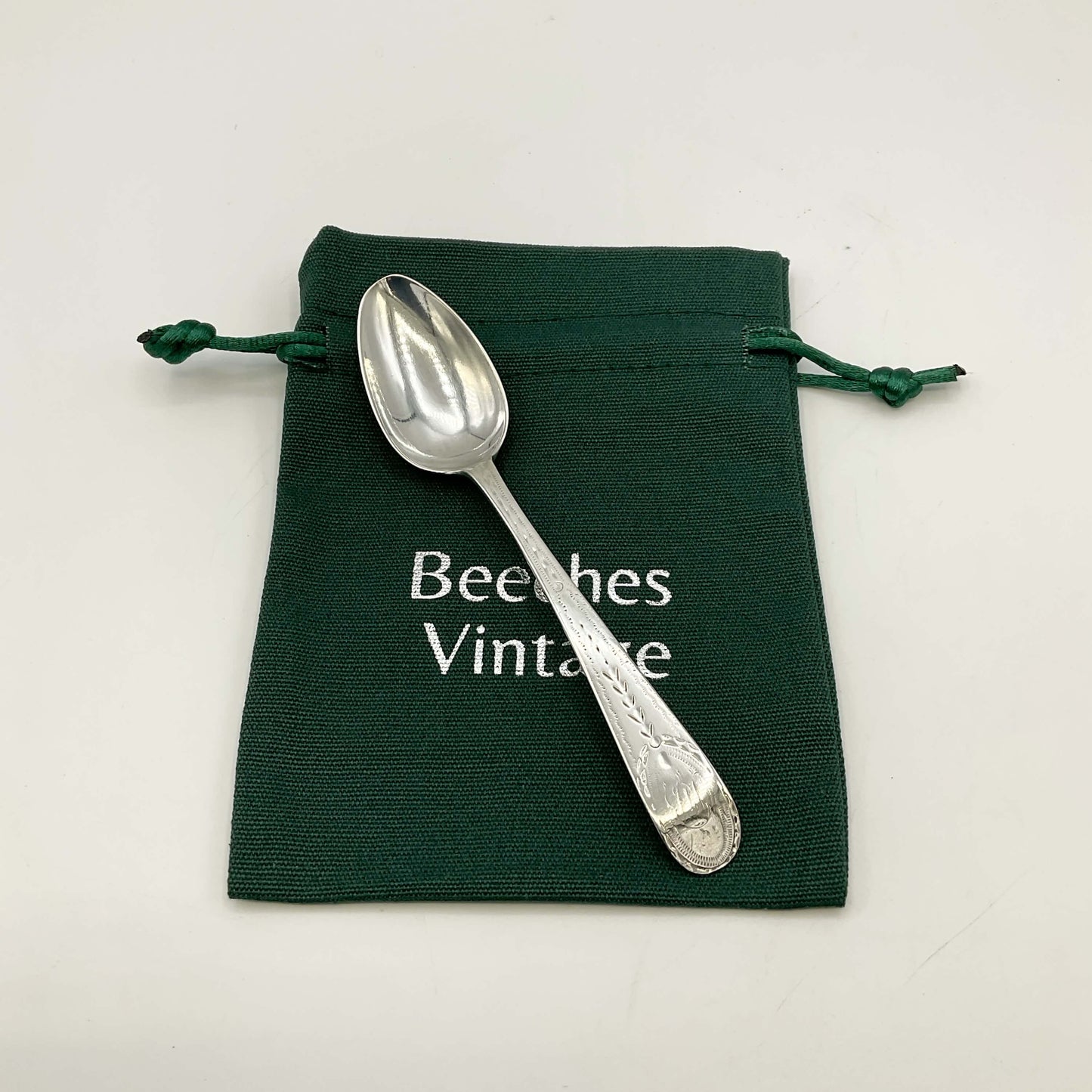 Silver spoon on a green drawstring bag with 'Beeches Vintage' text.