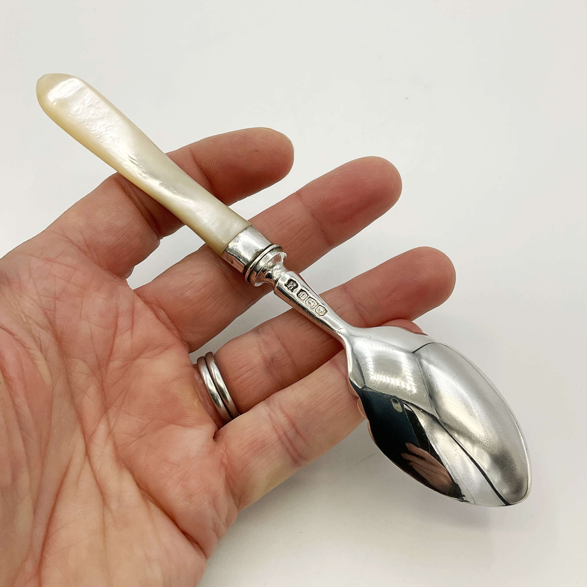 Hand holding a silver spoon with a decorative handle on a white background