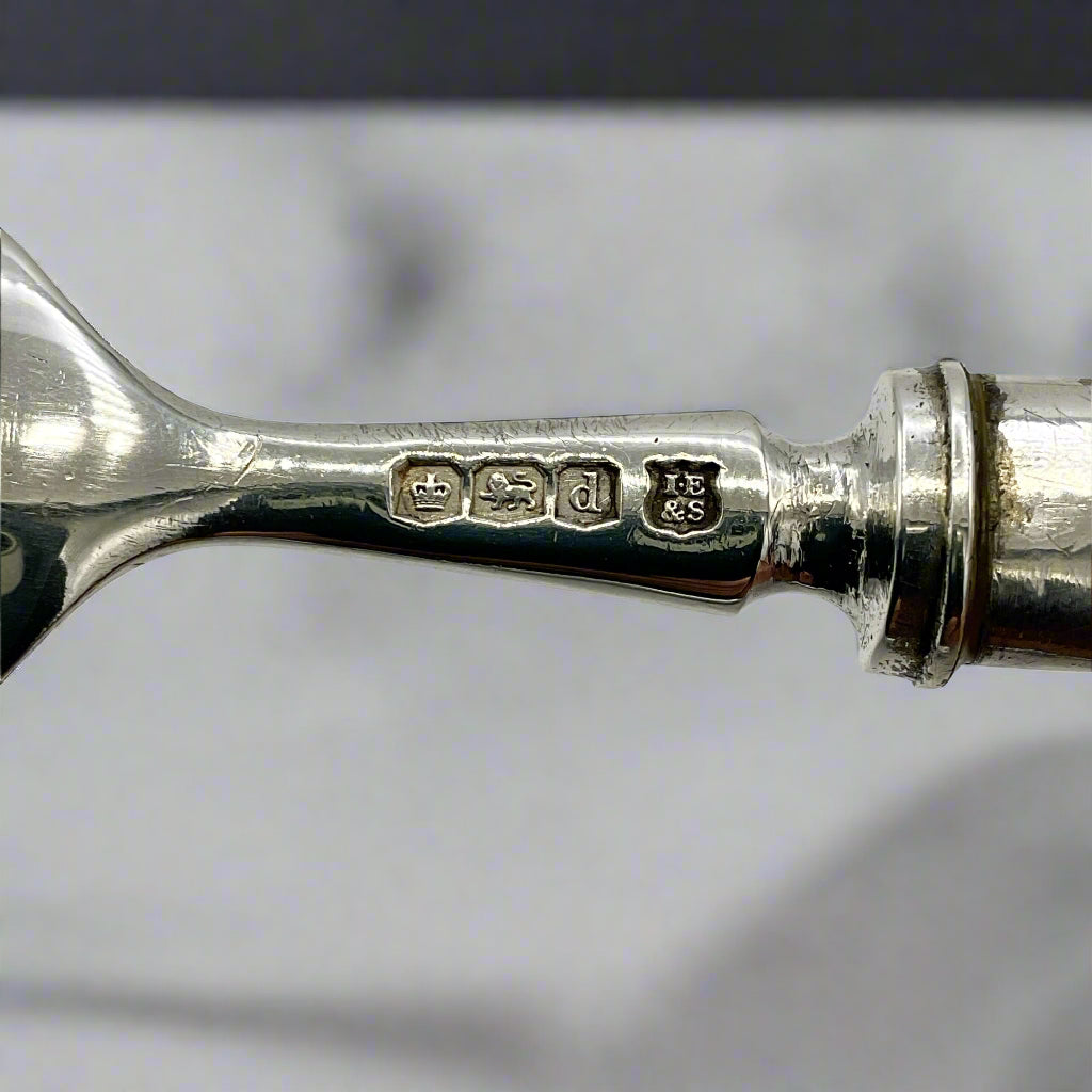 Close-up of a silver spoon with engraved hallmarks on a marble background 
