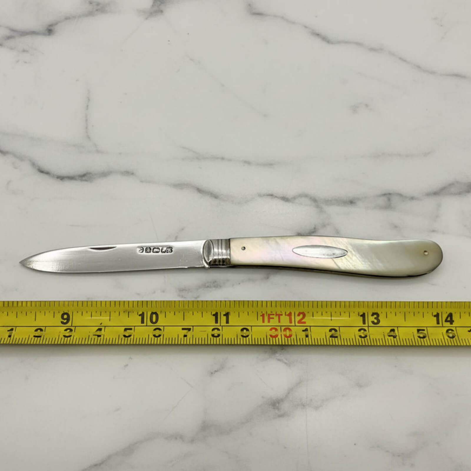 Knife with a decorative handle on a marble surface, measured by a tape measure.