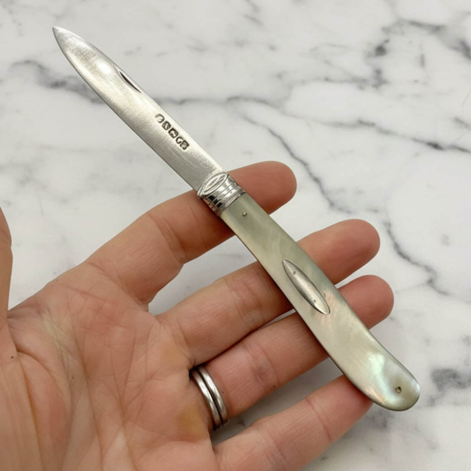 Silver pocket knife held in a hand against a marble background