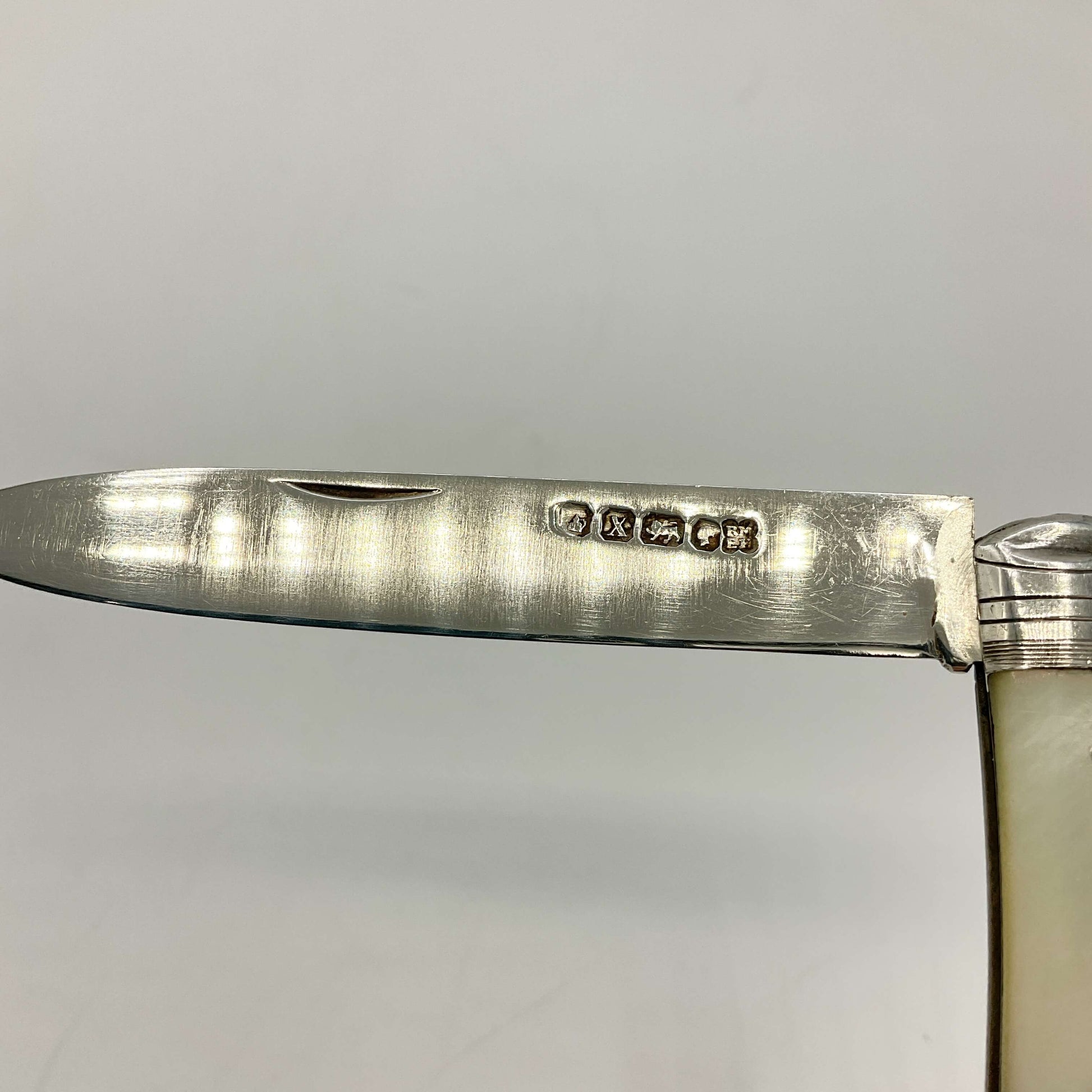 Close-up of a silver-handled knife with hallmark details on a light grey background