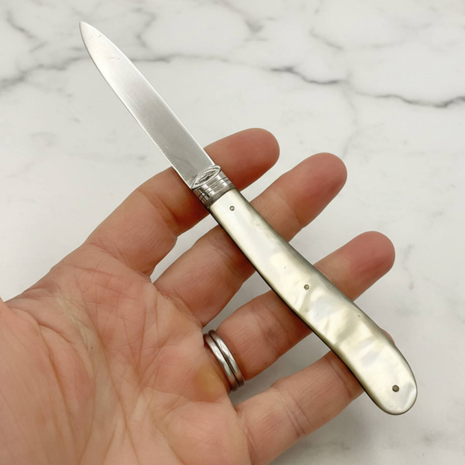 Folding knife with a decorative handle held in a hand against a marble background