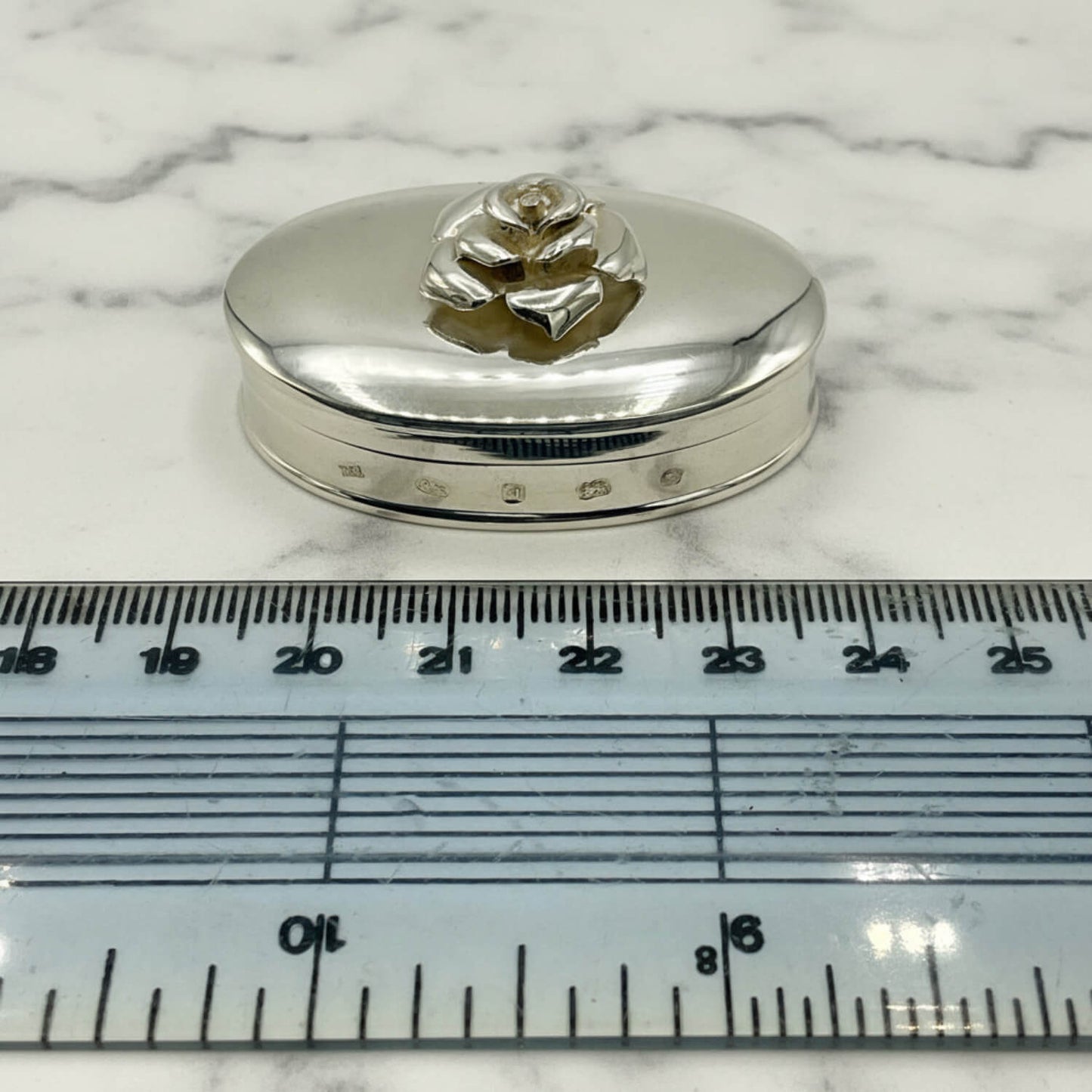 Large Rose Sterling Silver Pill Box next to a ruler for scale on a marble surface
