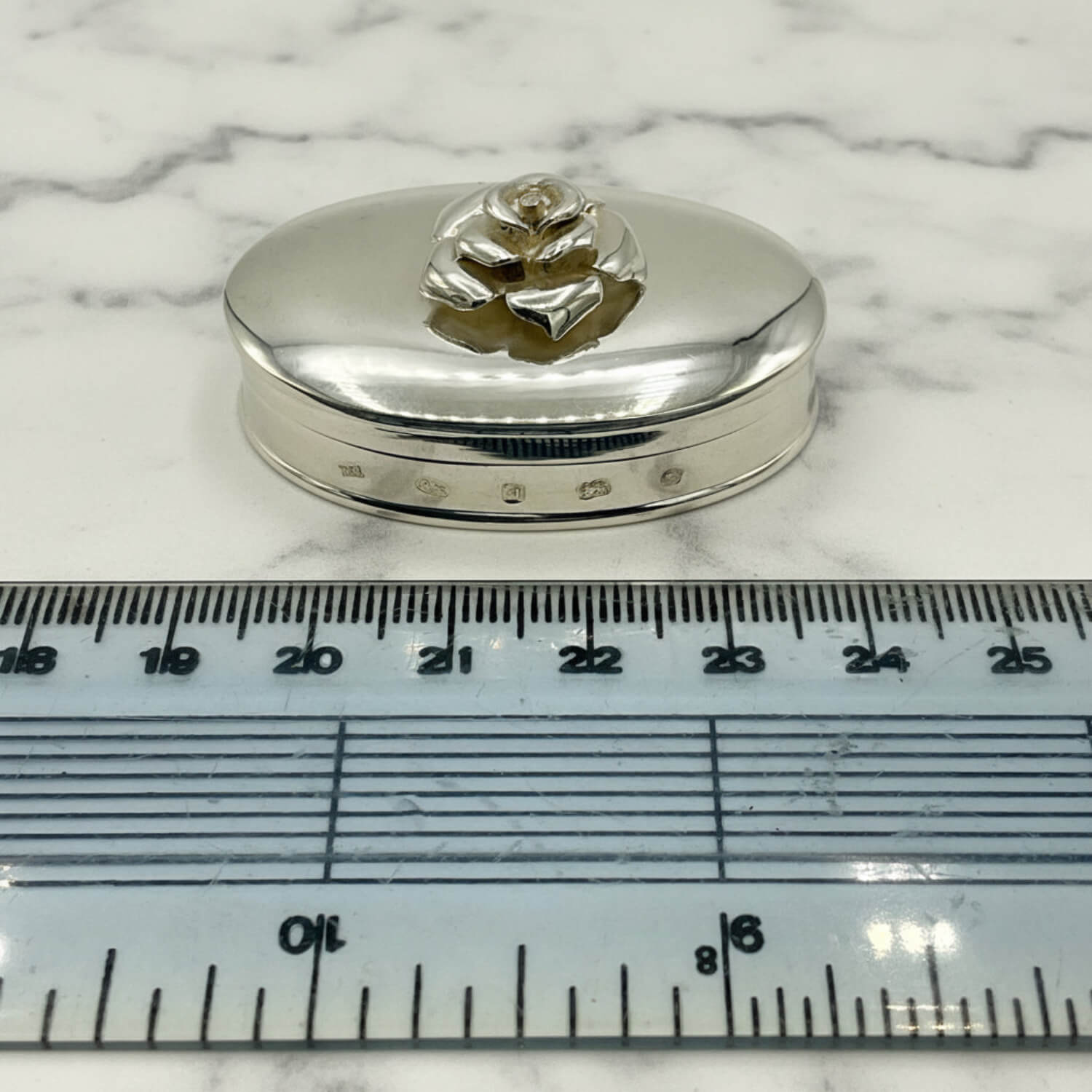 Large Rose Sterling Silver Pill Box next to a ruler for scale on a marble surface