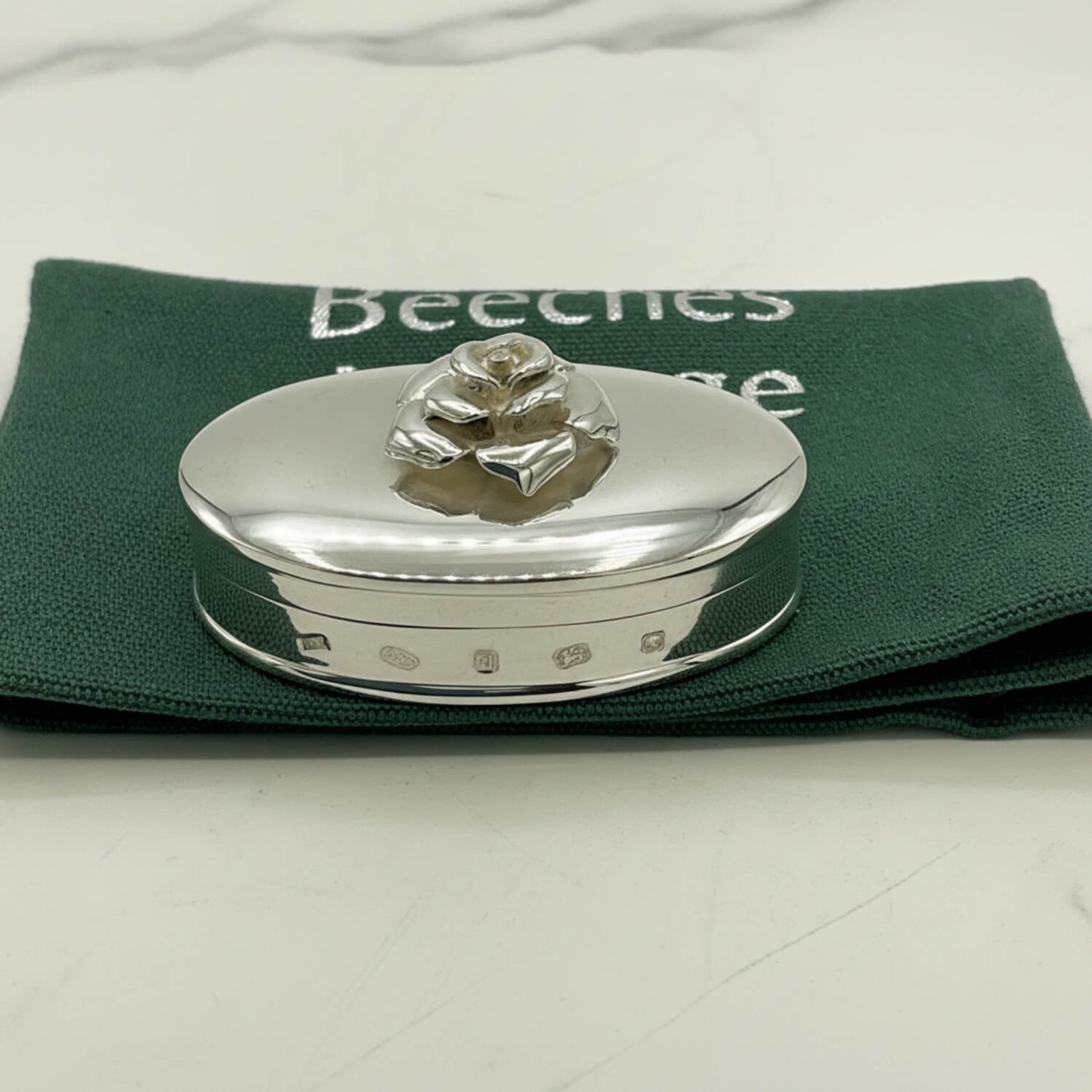 Silver trinket box with a decorative rose on a green cloth bag