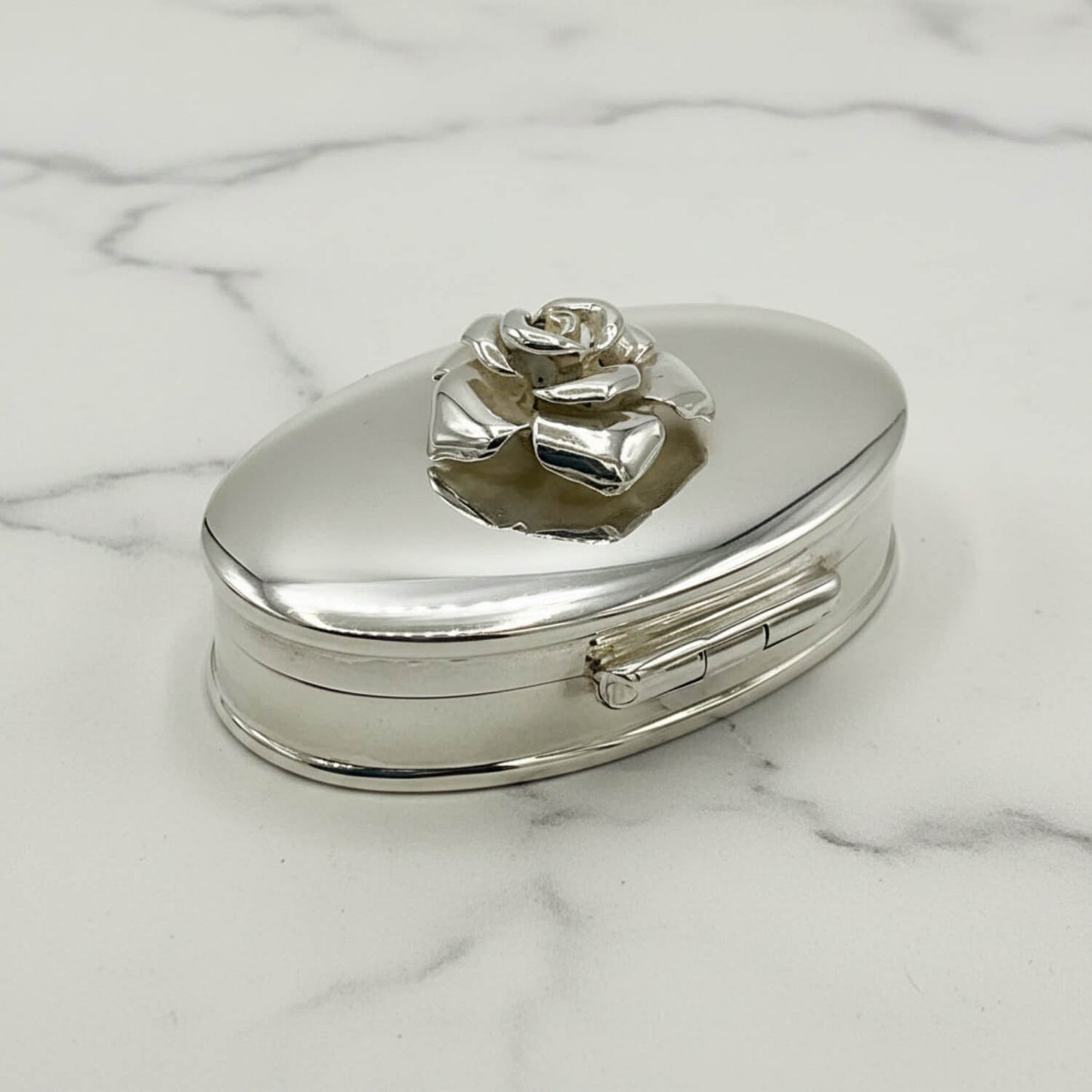 Silver pill box with a rose design on a marble surface