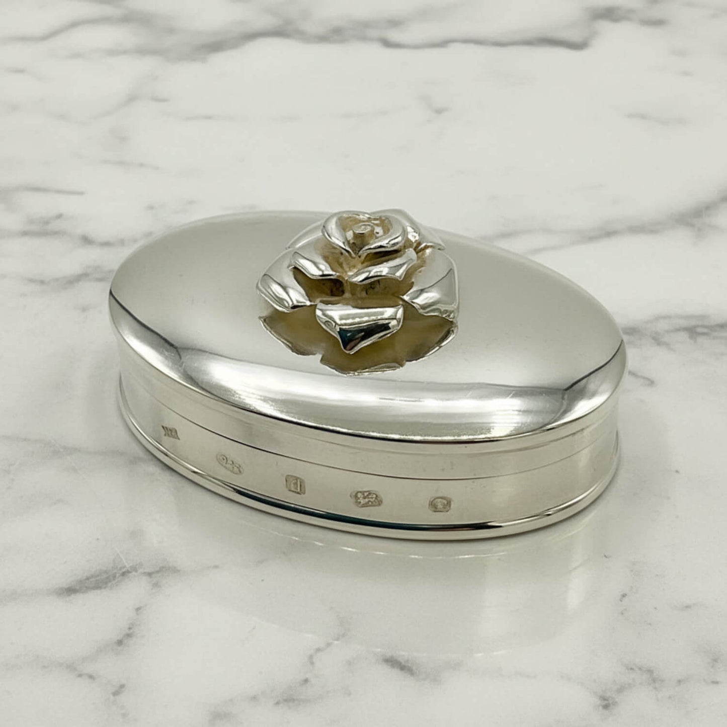Silver trinket box with rose design on a marble surface