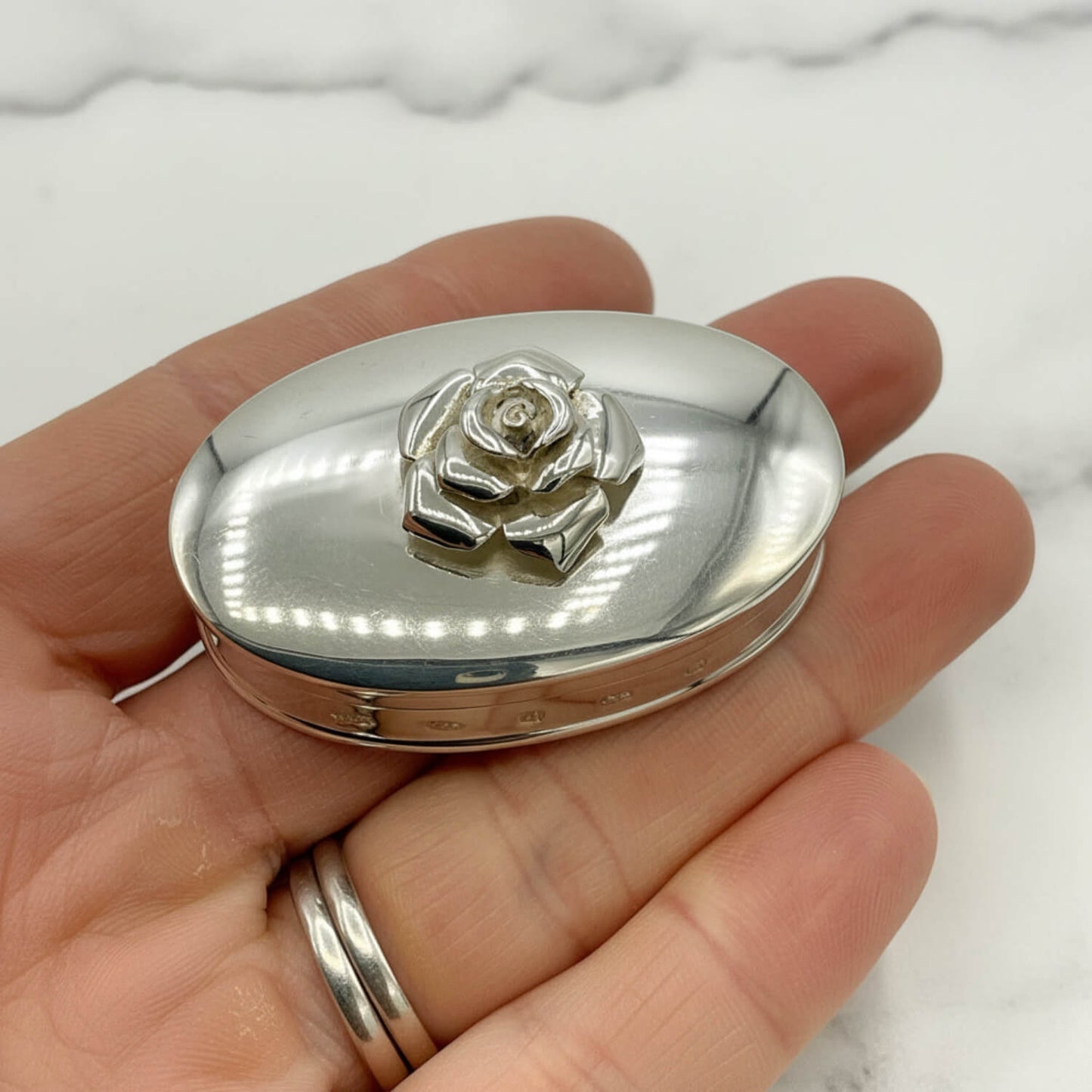 Large Rose Sterling Silver Pill Box held in a hand with a marble surface in the background