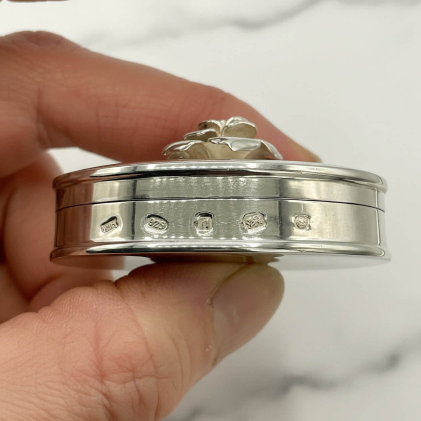 hallmarks on a Large Rose Sterling Silver Pill Box held in a hand with a marble background