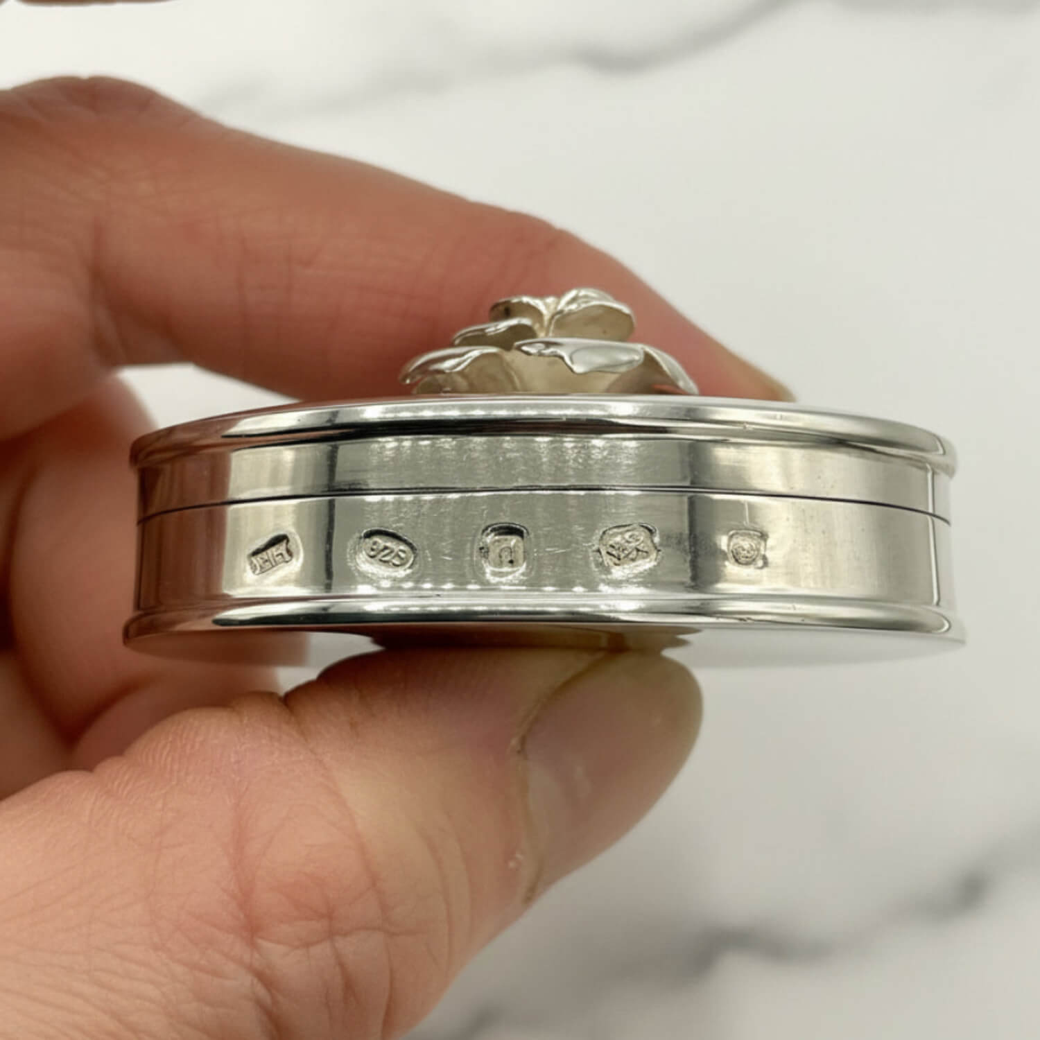 hallmarks on a Large Rose Sterling Silver Pill Box held in a hand with a marble background