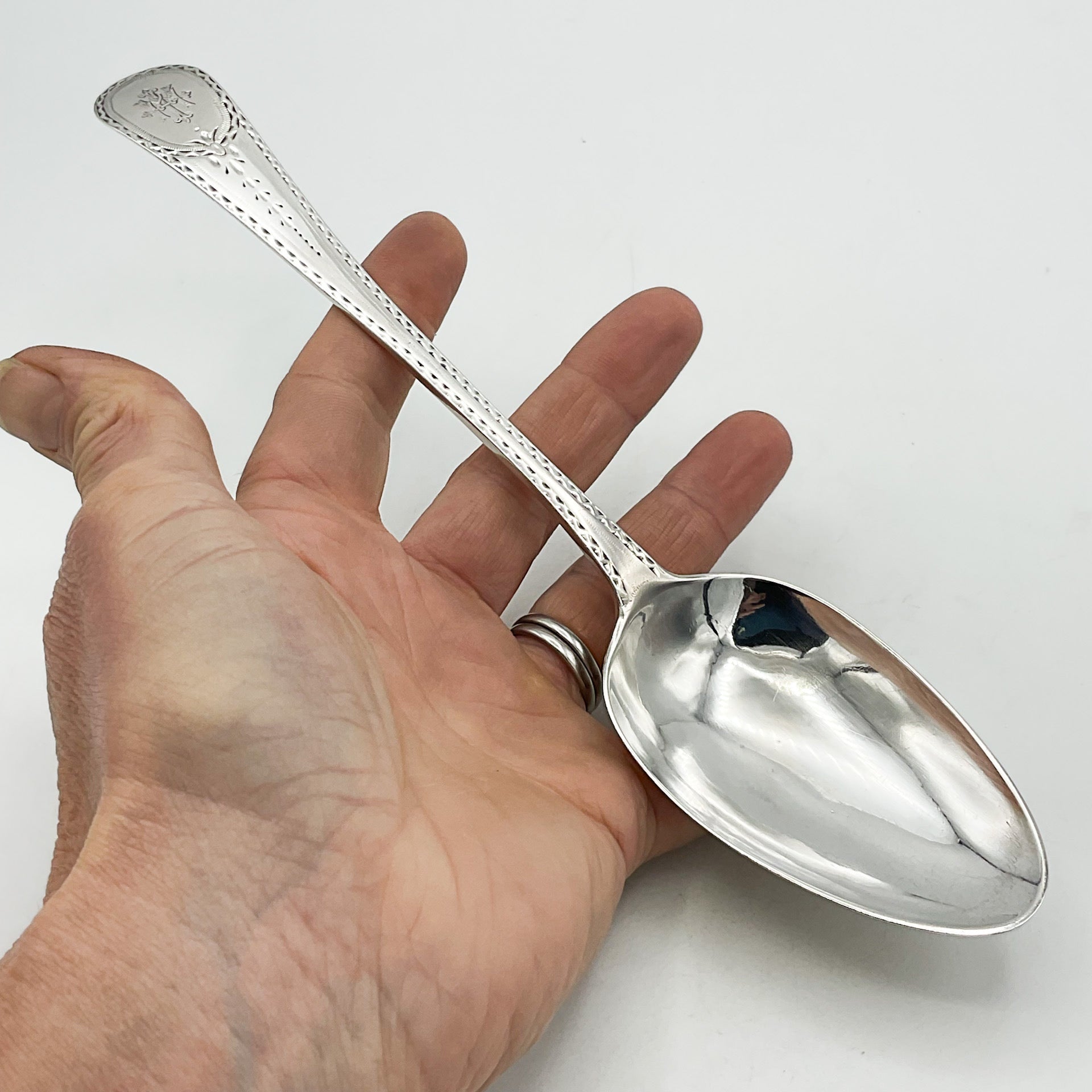 Large silver serving spoon held in a hand with a white background