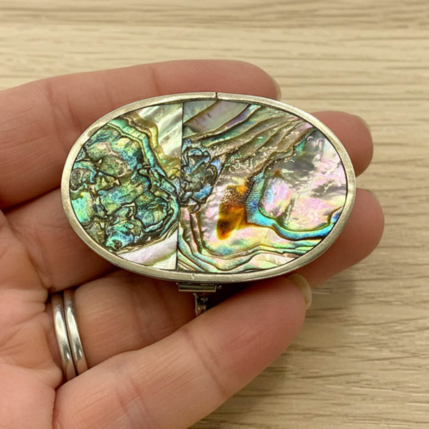 Mexican Abalone Shell Pill Box held in a hand with a wood table background