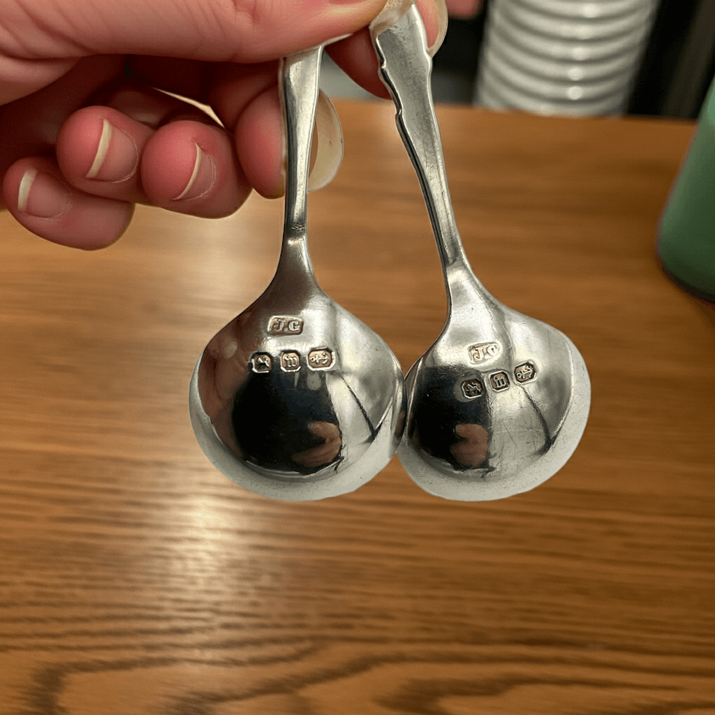 Two silver spoons held by a hand on a wooden surface