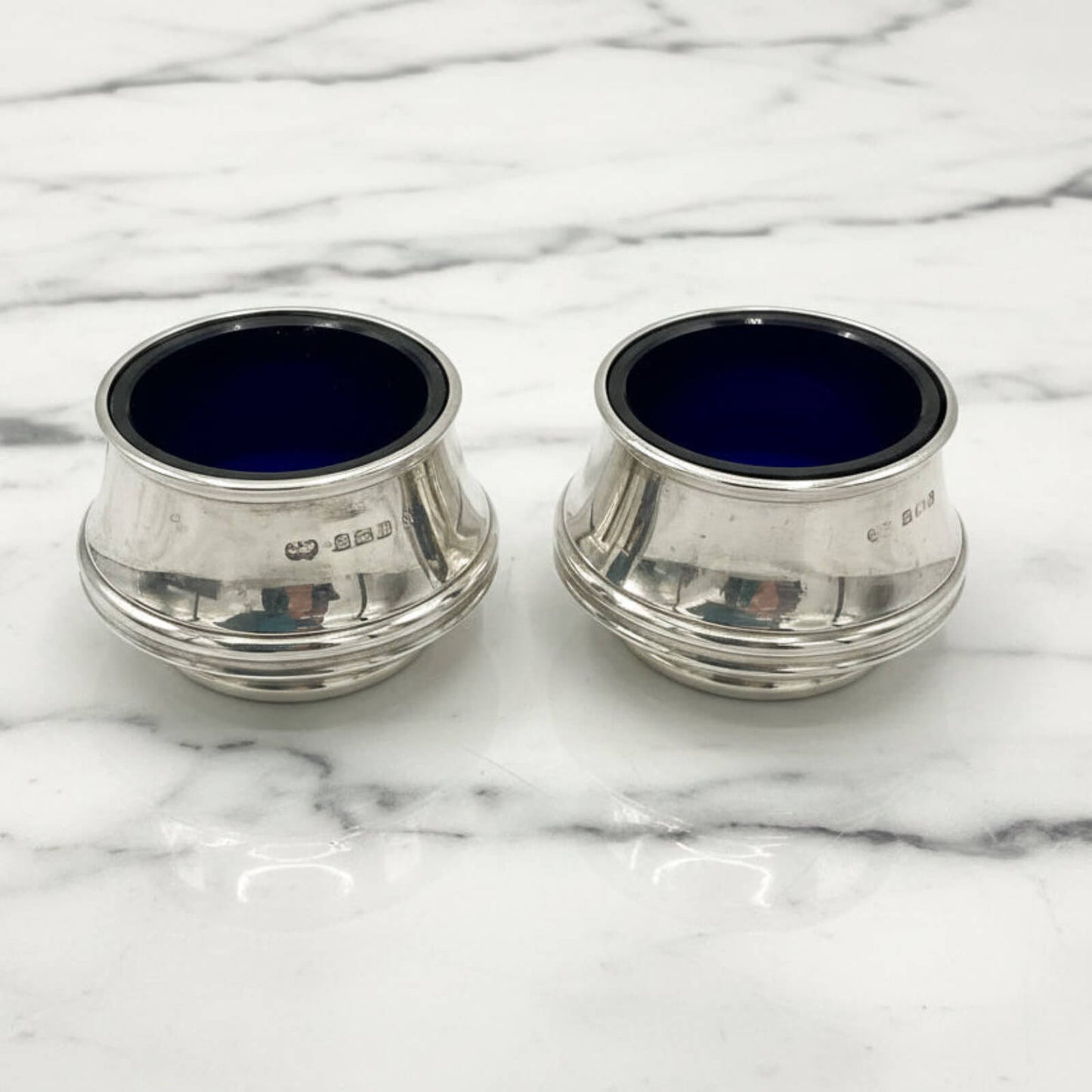 Two silver salts with blue liners on a marble surface