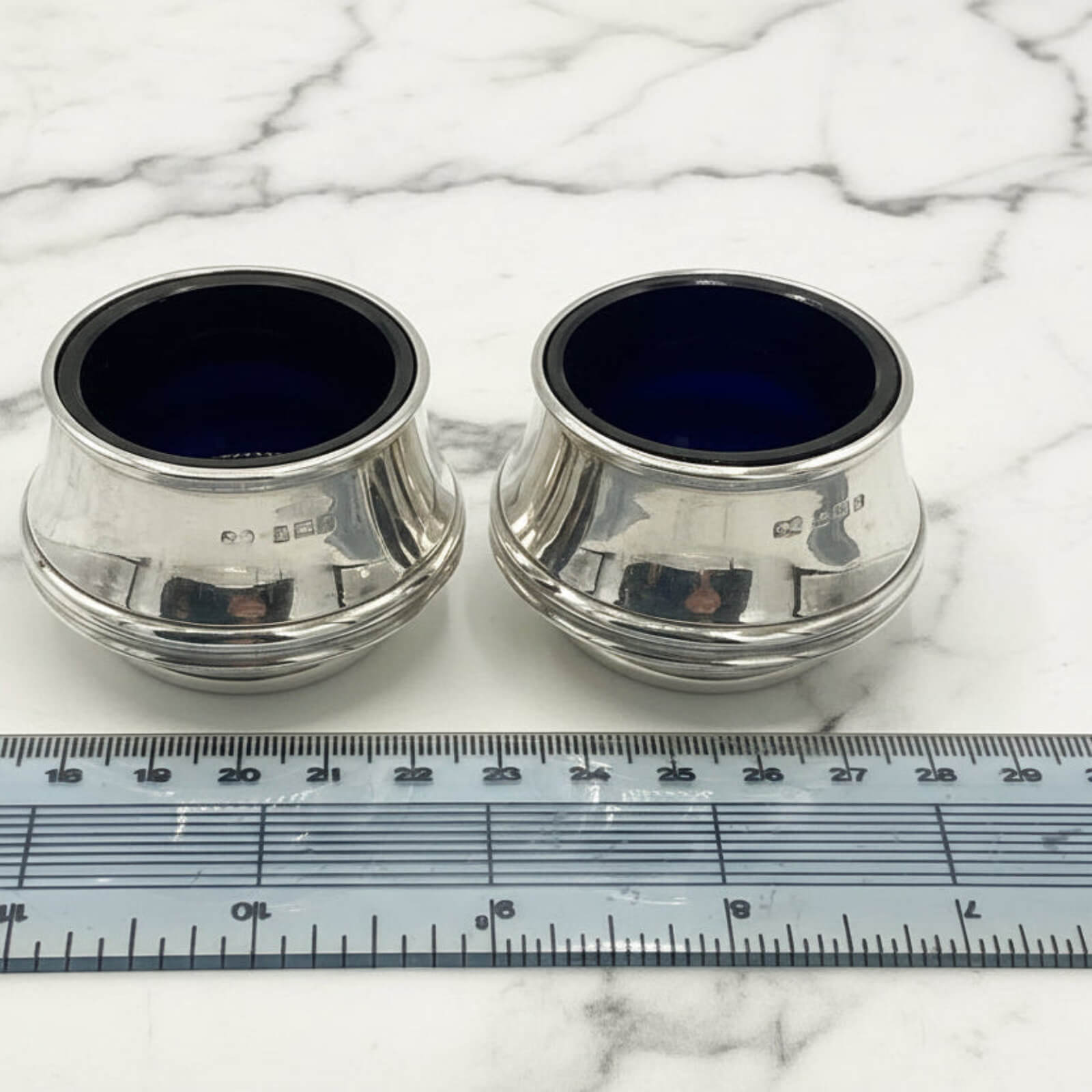 Two silver salts with blue interior on a marble surface with a ruler for scale.