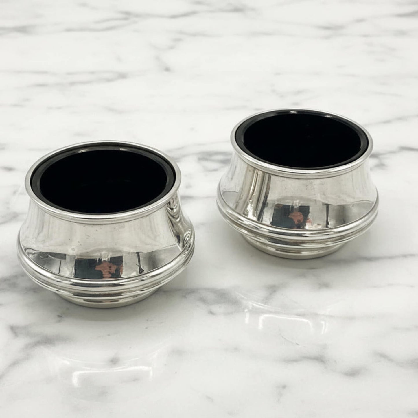 Two silver salts with blue liners on a marble surface