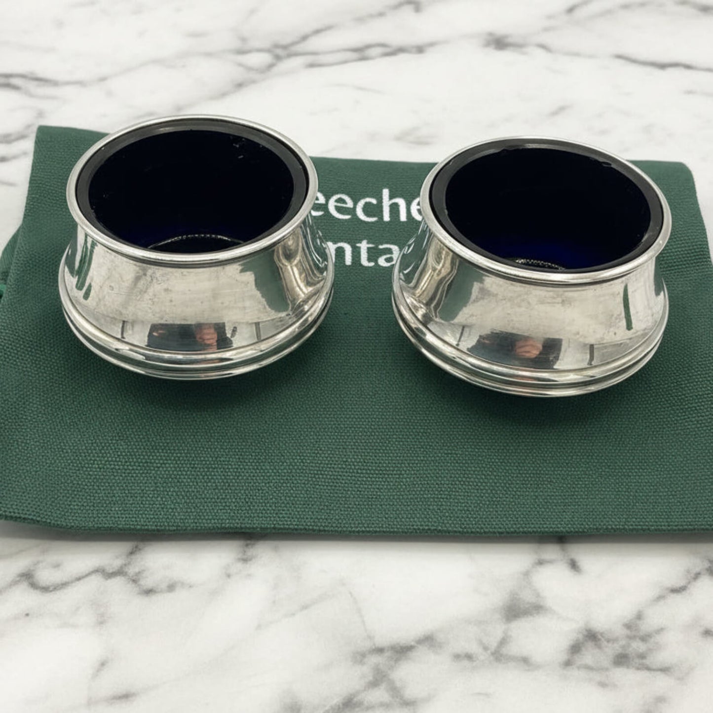 Two silver salt shakers on a green bag with a marble background