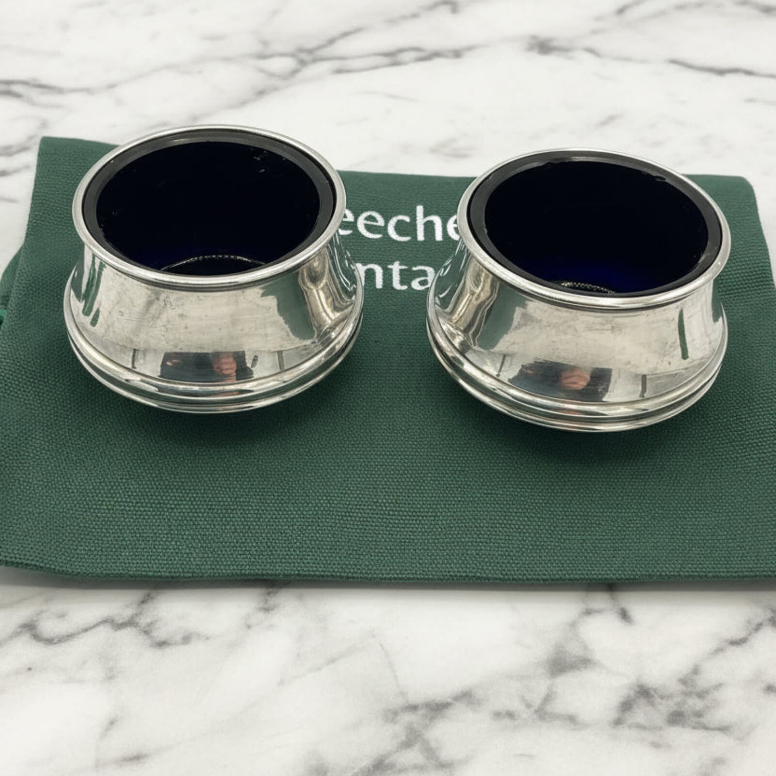 Two silver salt shakers on a green bag with a marble background