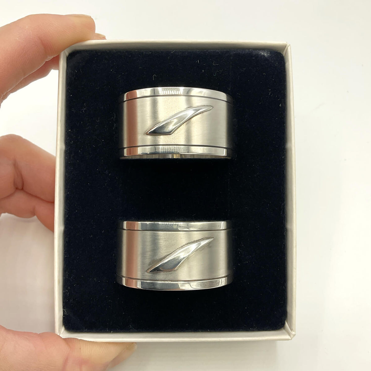Pair of Concorde Sterling Silver Napkin Rings displayed in a black velvet-lined gift box held by a hand against a white background.