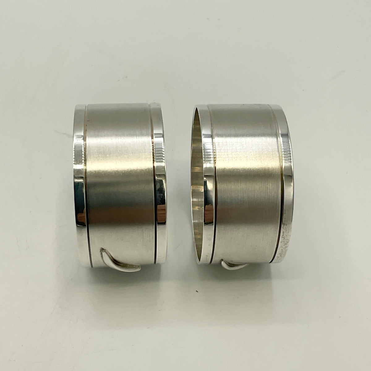 Two brushed silver napkin rings with polished edges and small loop details, displayed side by side on a plain light background.