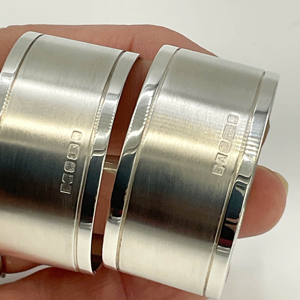 Pair of Concorde Sterling Silver Napkin Rings with brushed and polished finishes showing hallmarks, held side-by-side on a person's fingers against a white background.