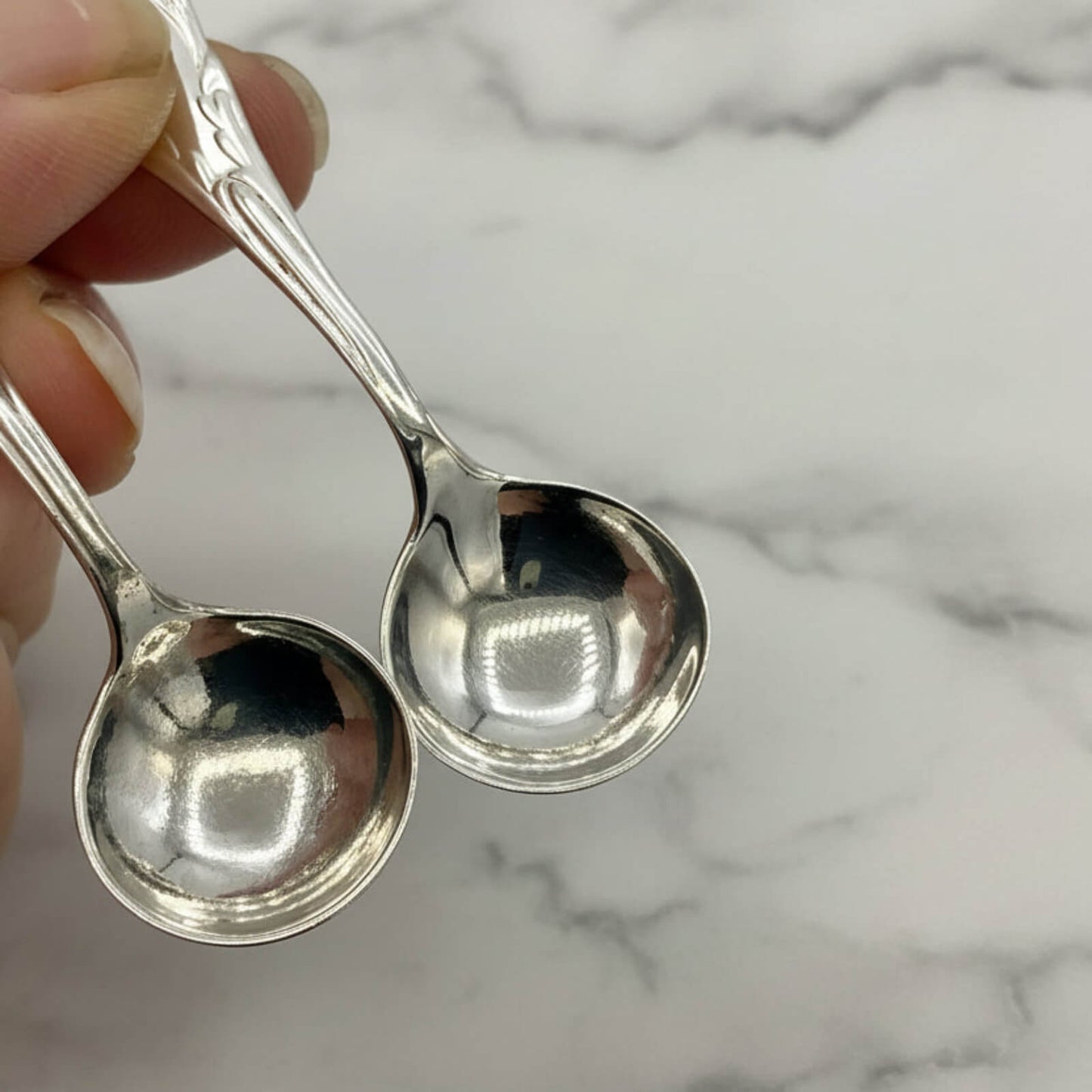Two silver spoons held by a hand against a marble background