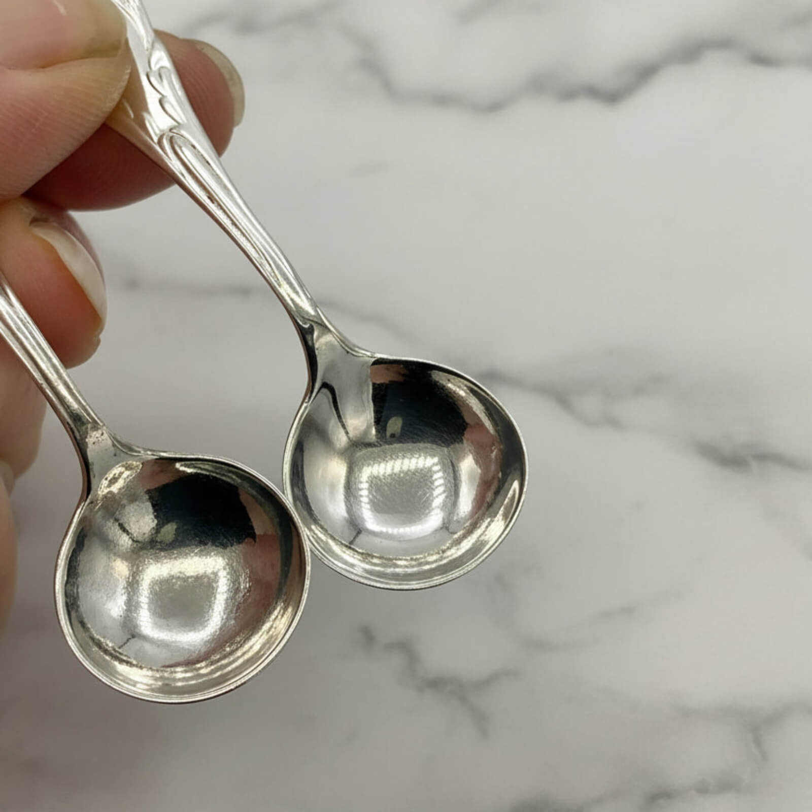 Two silver spoons held by a hand against a marble background