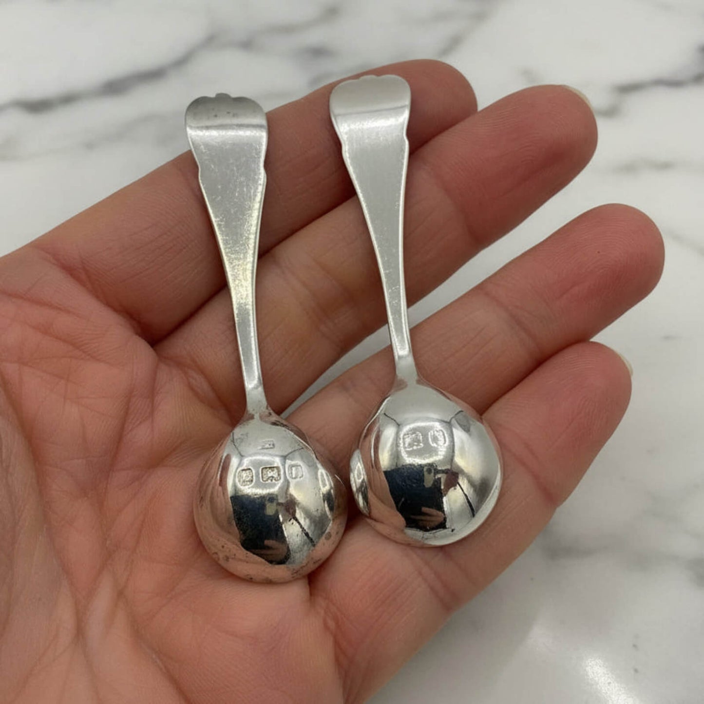 Two silver spoons held in a hand with a marble background