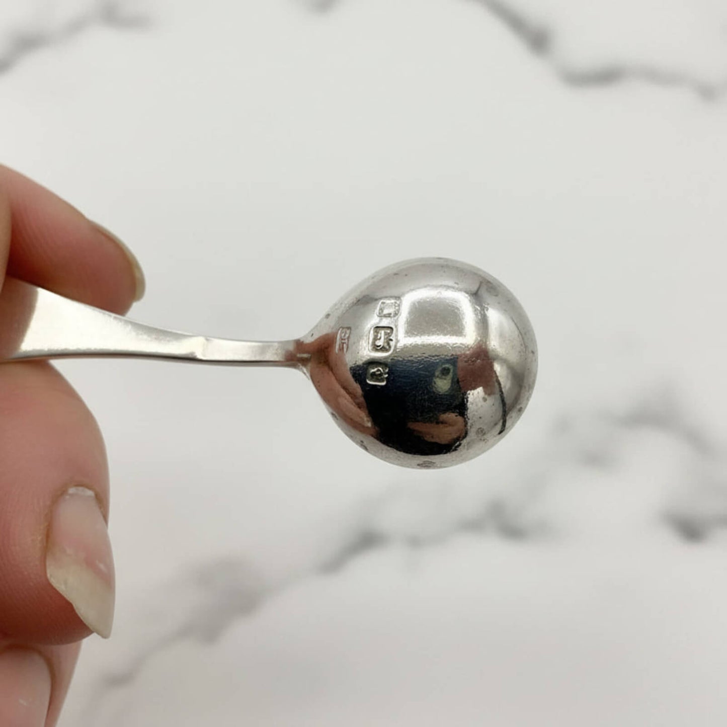 Silver spoon held by a hand with a blurred marble background