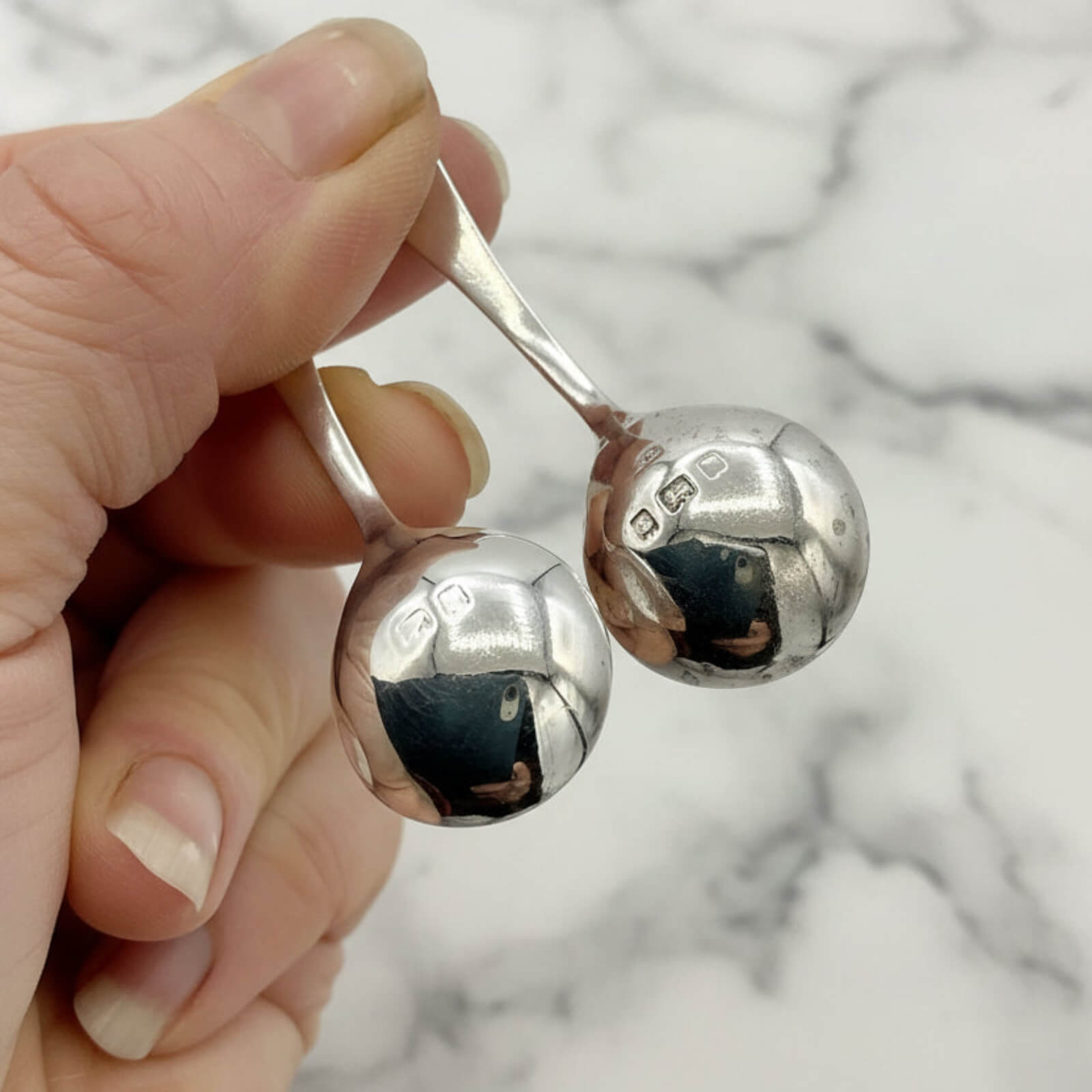 Hand holding two silver salt spoons against a marble background
