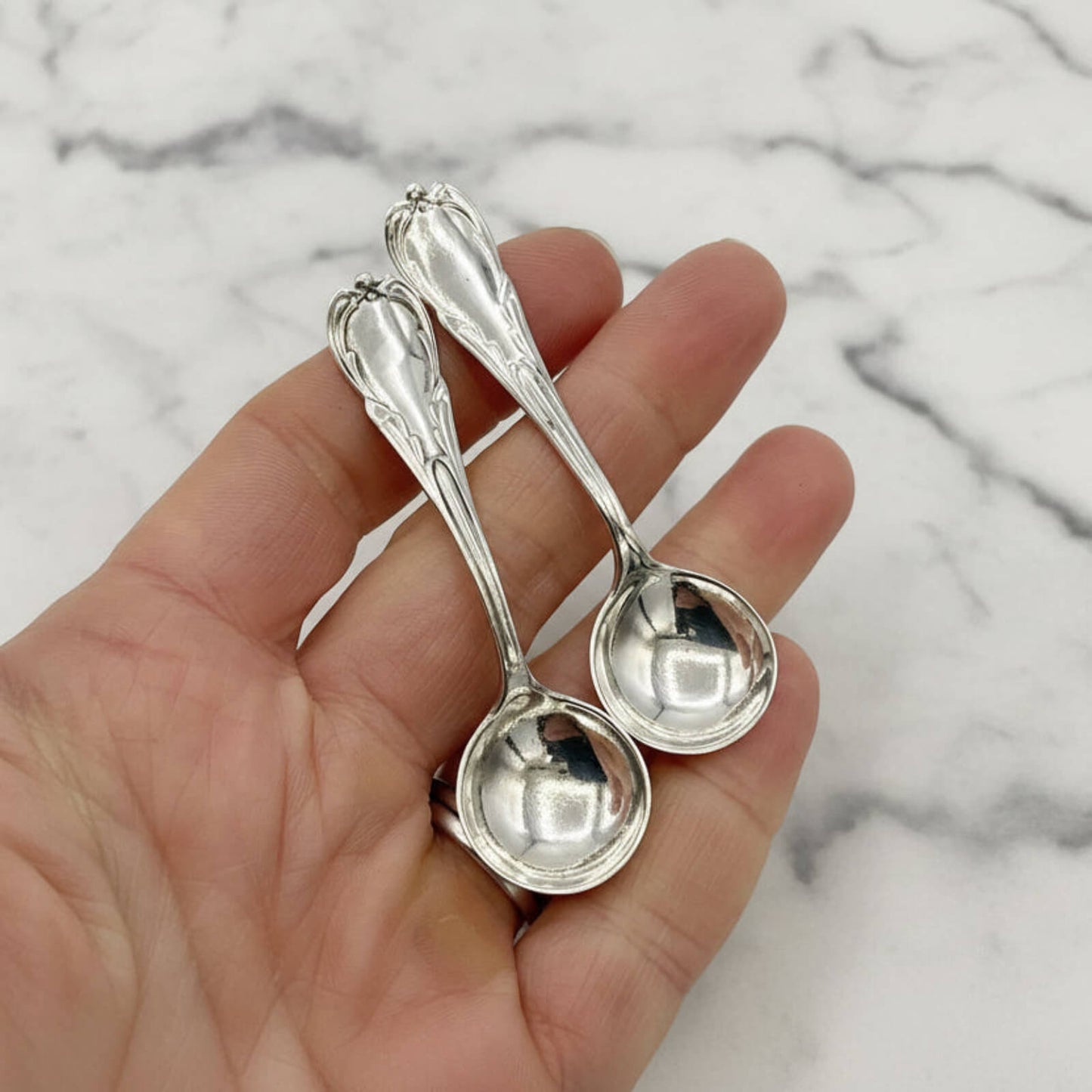 Two silver spoons held in a hand against a marble background