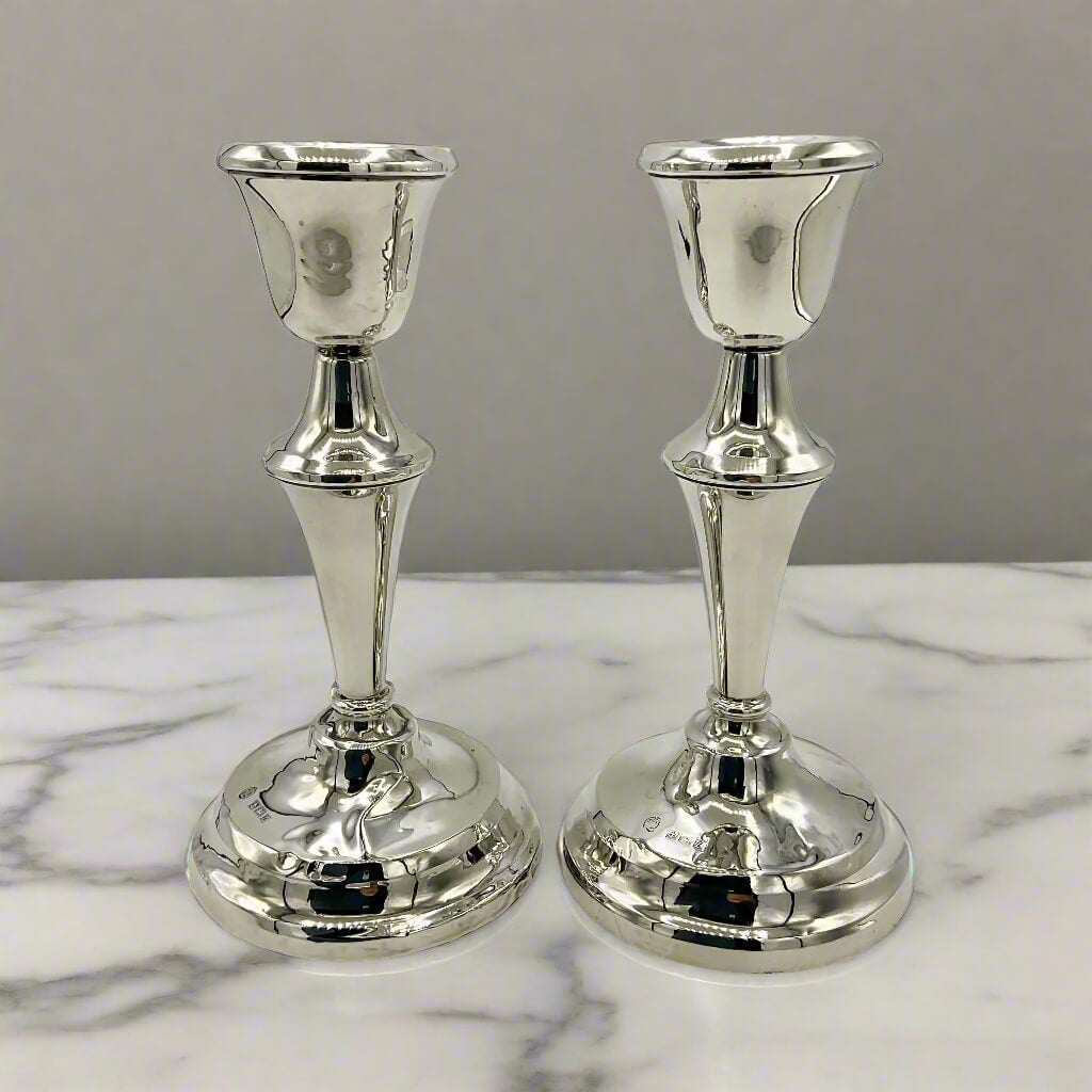 Two silver candle holders on a marble surface with a gray background