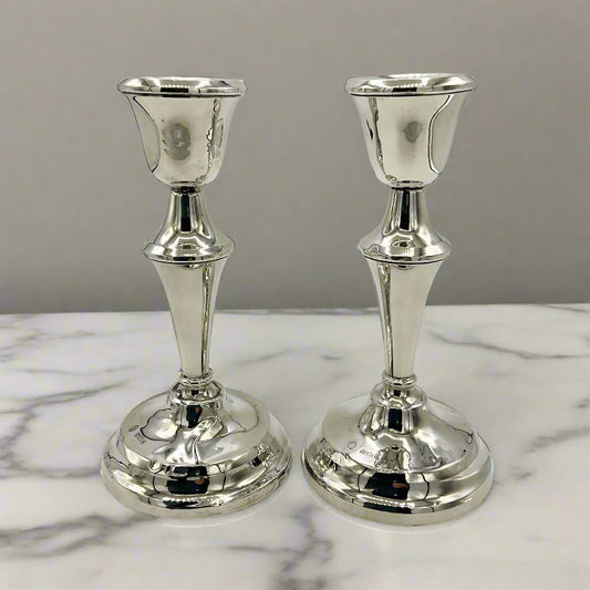Two silver candle holders on a marble surface with a gray background