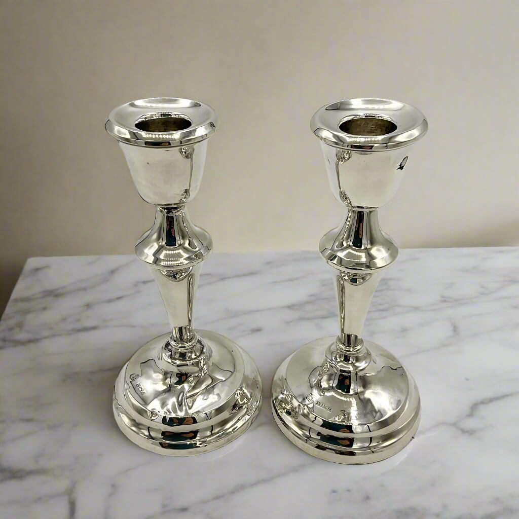 Two silver candle holders on a marble surface with a neutral background