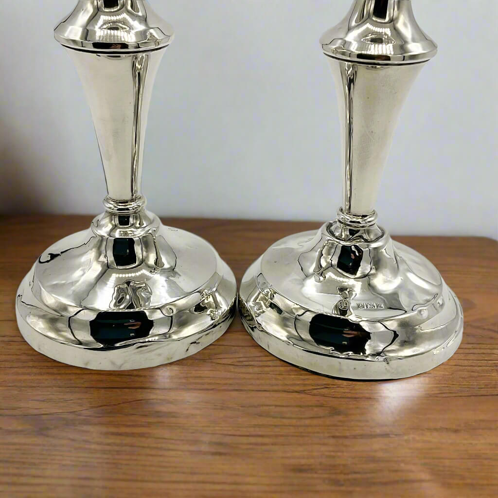 Two silver candle holders on a wooden surface with a plain background