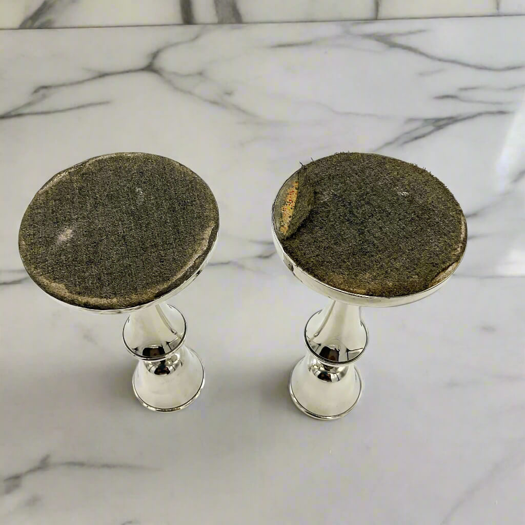 Two silver candle holders with dark candle bases on a marble surface