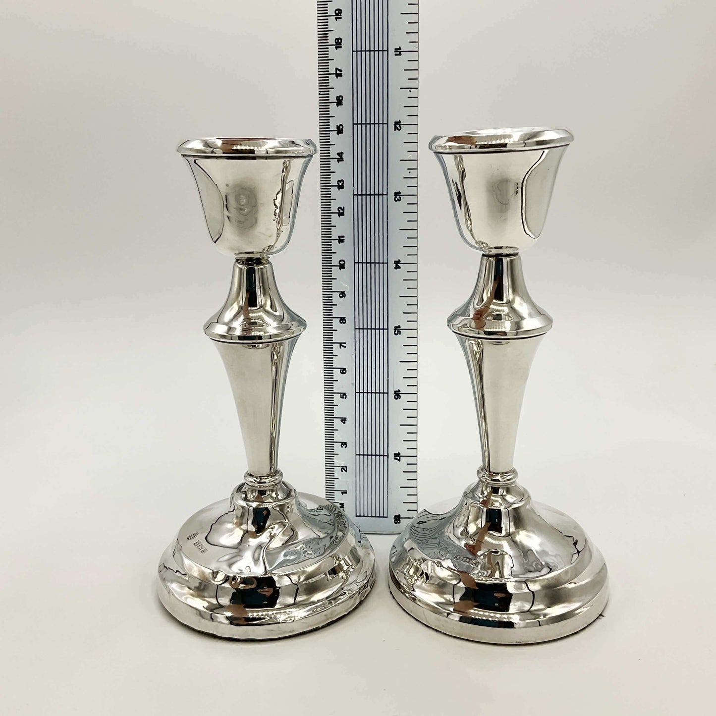 Two silver candle holders with a ruler for scale on a white background