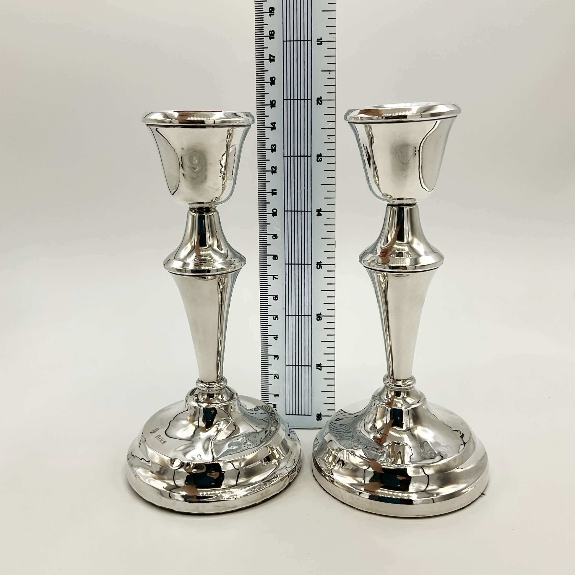 Two silver candle holders with a ruler for scale on a white background