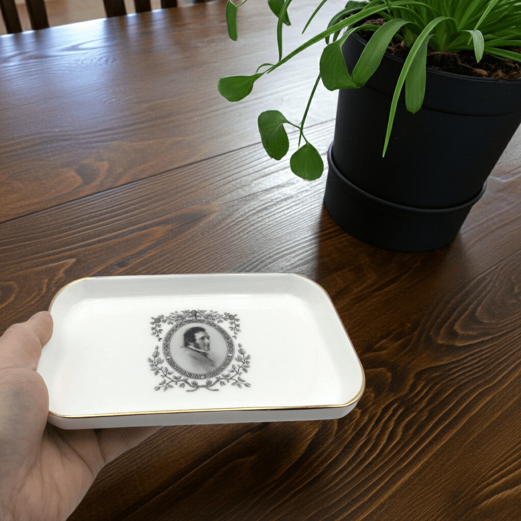 White tray with black design held by a hand on a wooden table with a plant in the background
