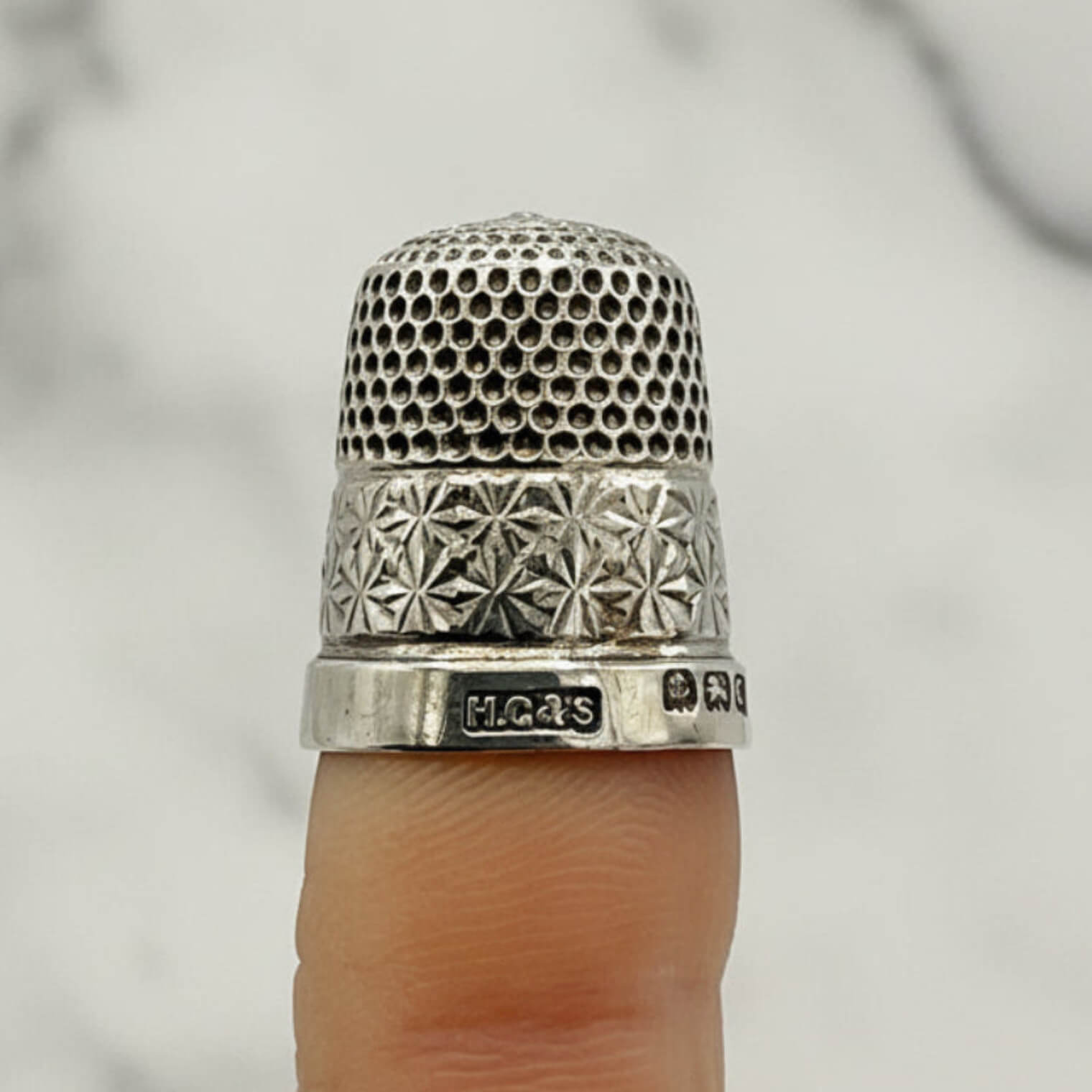 Silver thimble on a finger showing hallmarks