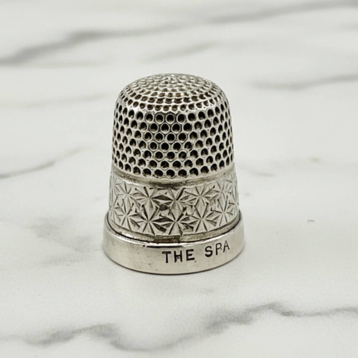 Silver thimble with intricate patterns on a marble surface