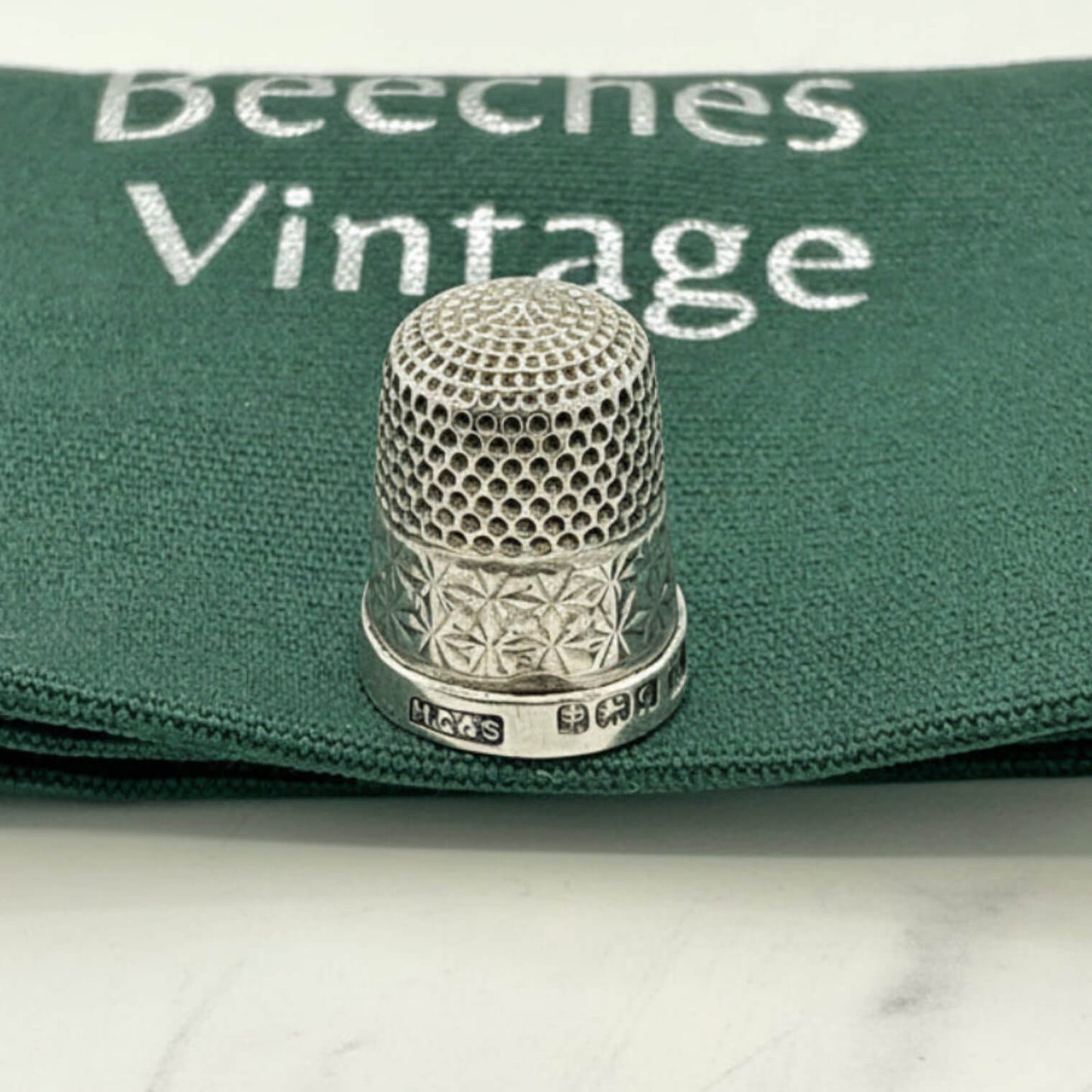 Silver thimble on a green fabric with 'Beeches Vintage' branding