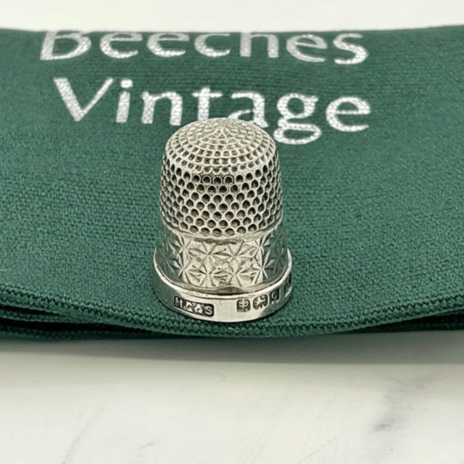 Silver thimble on a green fabric with 'Beeches Vintage' branding