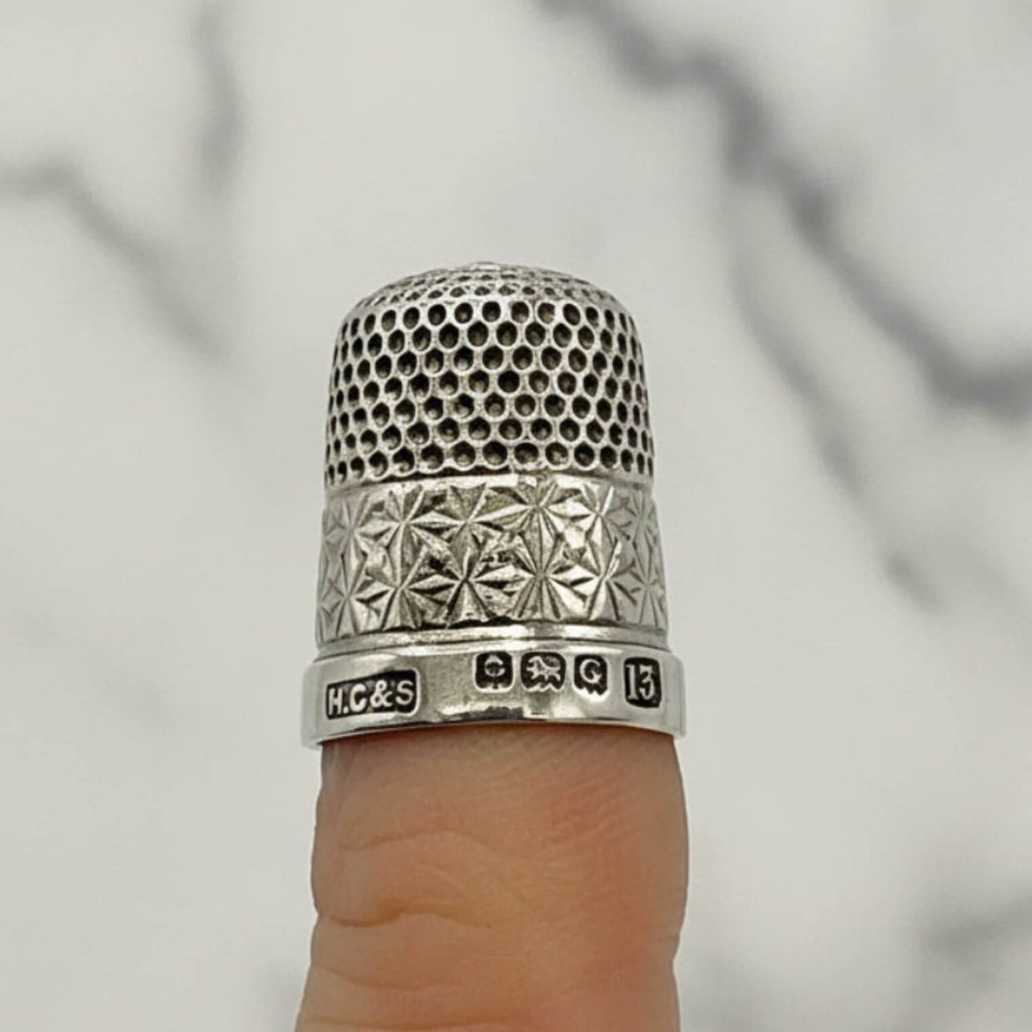 Silver thimble on a finger with a blurred background