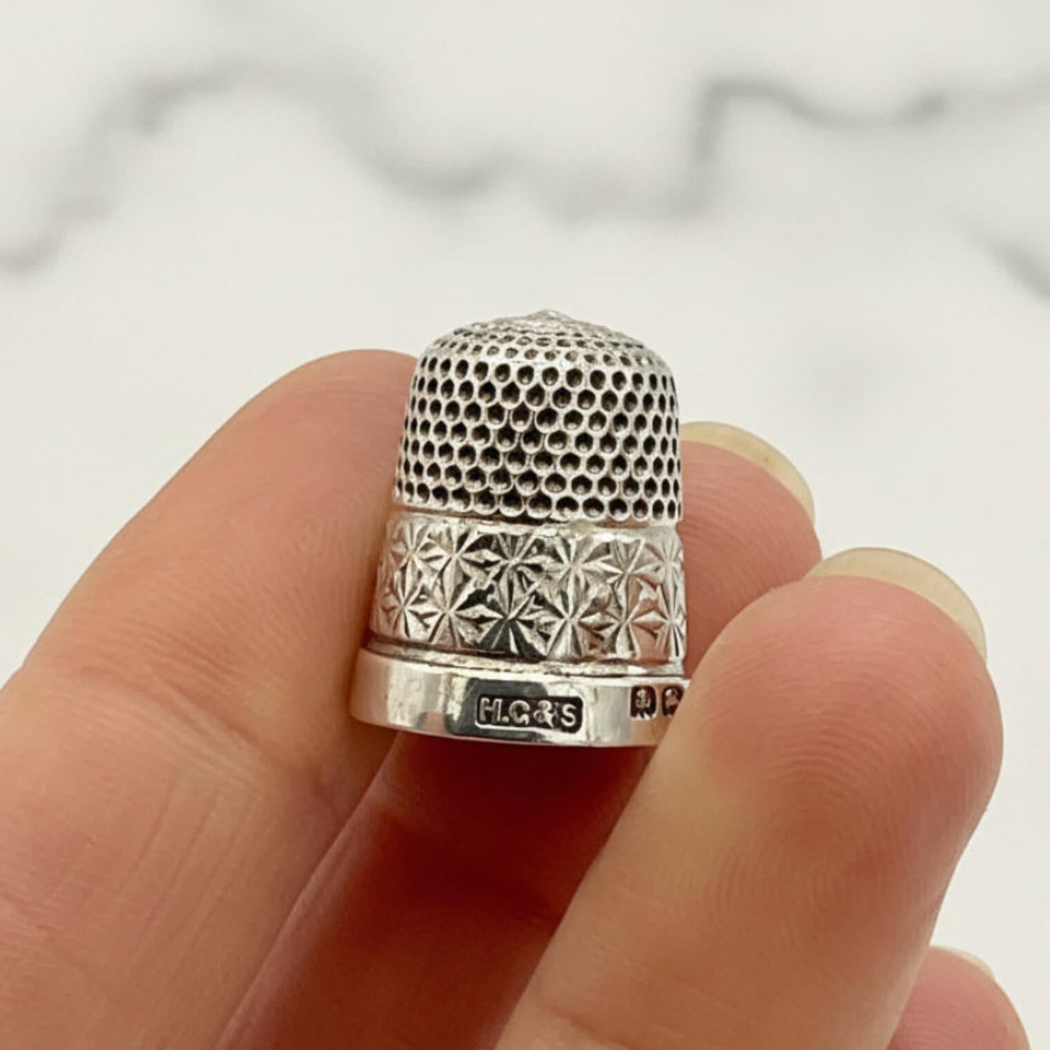 Silver thimble held on a finger against a neutral background