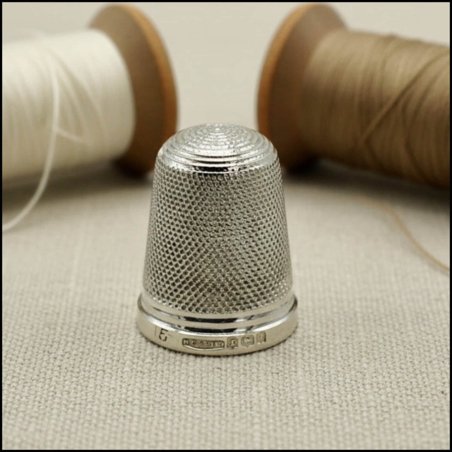 Silver thimble on a fabric surface with spools of thread in the background