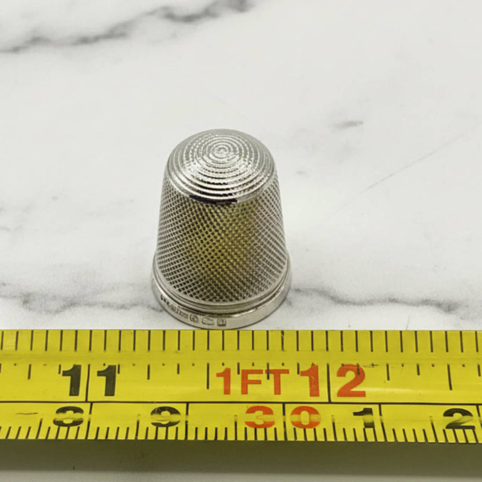 Silver thimble on a marble surface with a measuring tape for scale.
